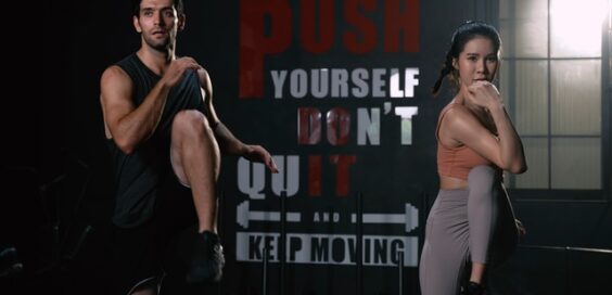 A young man and woman exercise in front of a sign that reads "PUSH YOURSELF DON'T QUIT AND KEEP MOVING."