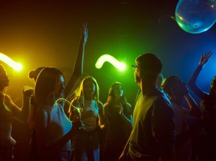 A group of students dances as they celebrate in a dimly lit room filled with colorful neon lights and decorations.