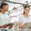 Two college women are conversing in a building, smiling and glancing at their notebooks and tablets.