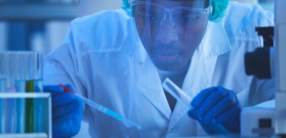 A close-up of a young man in a laboratory wearing protective gear and holding scientific instruments for an experiment.