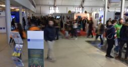 A crowded indoor professional event with attendees walking past booths, signage, and a brochure display stand.