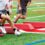 A close-up of the feet of three young athletes navigating around red barriers on a football field for a drill.