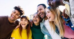 A group of six older students stand together happily and smiling as they take a group selfie on a school trip.