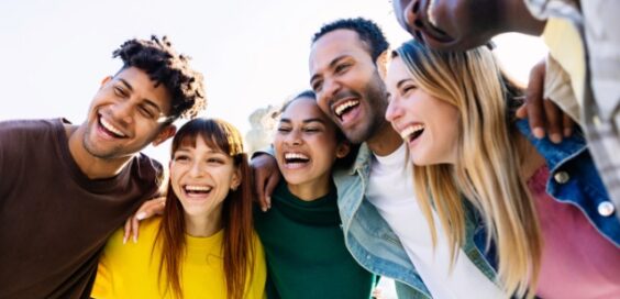 A group of six older students stand together happily and smiling as they take a group selfie on a school trip.