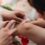A close-up of a little kid with a knee scrape. Someone sprays something on the cut and holds a tissue near it.