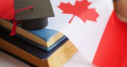 Black graduation cap rests on stacked books beside a red and white Canadian flag with a prominent maple leaf.