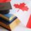 Black graduation cap rests on stacked books beside a red and white Canadian flag with a prominent maple leaf.