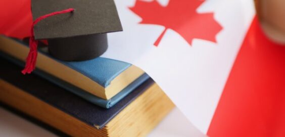 Black graduation cap rests on stacked books beside a red and white Canadian flag with a prominent maple leaf.