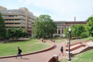 A college campus features a large brick walkway with students walking to the large brick buildings.