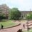 A college campus features a large brick walkway with students walking to the large brick buildings.