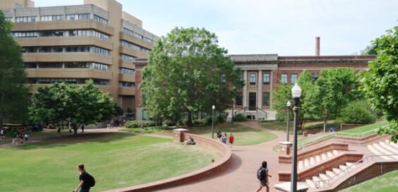 A college campus features a large brick walkway with students walking to the large brick buildings.