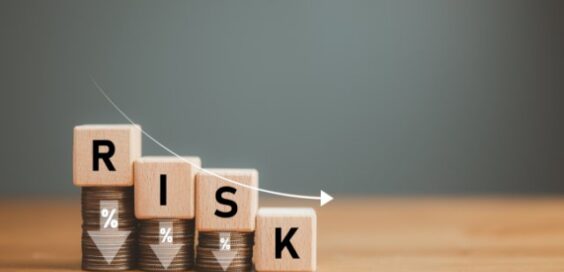 A close-up of four wooden blocks with letters on descending stacks of coins. The letters spell out "RISK."