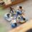 Downward view of five students sitting in a circle on the floor. They have notebooks, a laptop, and a tablet.