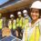 A close-up of a woman in a hard hat standing in front of people wearing safety gear in an outdoor area.