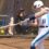A young female softball player in a white and blue uniform and a white batting helmet is swinging at a softball pitch.