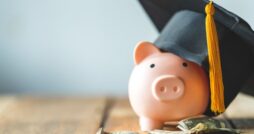 A piggy bank wearing a graduation cap surrounded by cash and coins.