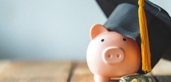 A piggy bank wearing a graduation cap surrounded by cash and coins.